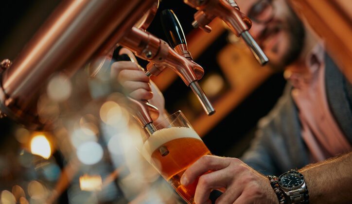 Close up of bartender standing in bar and pouring beer from tap.