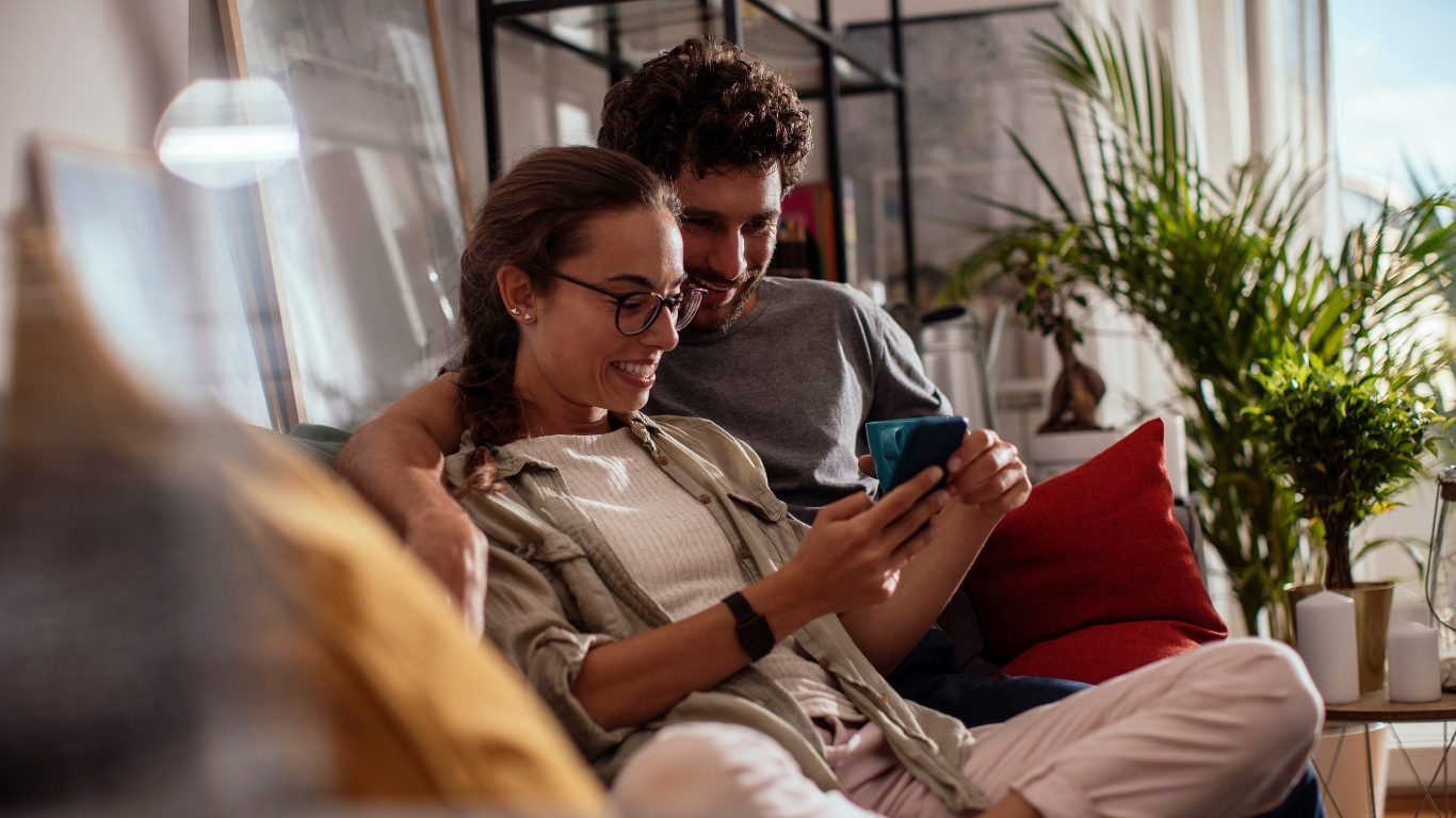 Young woman using her phone while relaxing with her boyfriend at their home