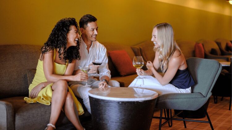 Three friends sitting down in restaurant laughing with a glass of wine in their hands.