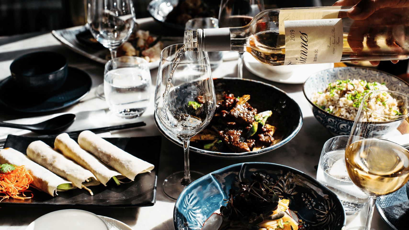 Wine pouring into a glass with dishes in the background
